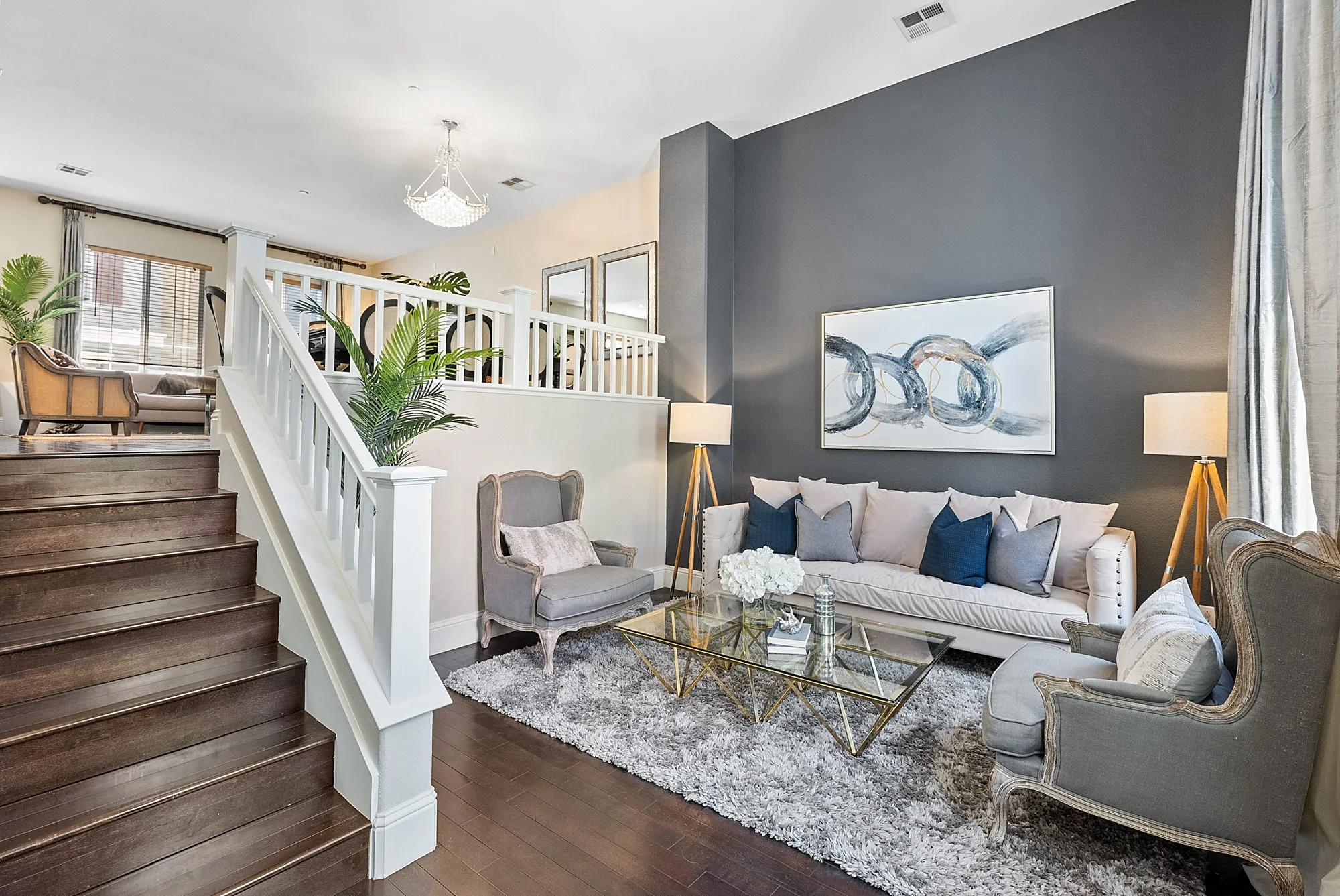 A staged living room in a Livermore townhome, a white staircase rising past a grey accent wall and two armchairs